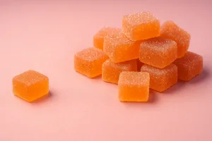 Orange sugar-coated cannabis gummies stacked on a pink background