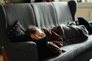 Person sleeping peacefully on a couch wrapped in a blanket indoors